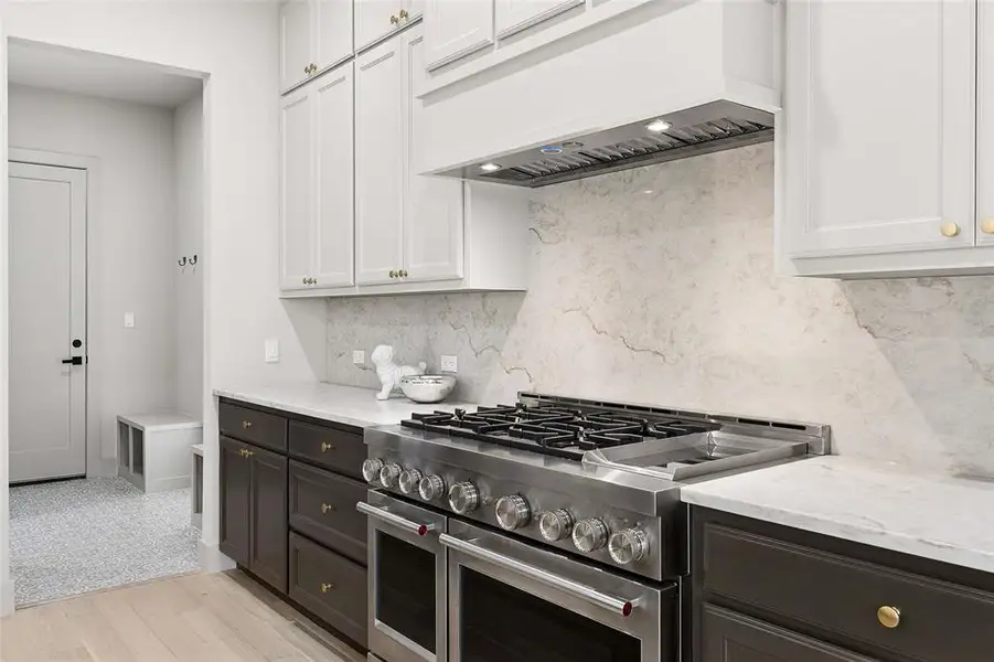 Stainless steel commercial grade range with multiple burners and double ovens, complemented by a matching range hood. Taj Majol countertops and backsplash. Stainless steel commercial grade range with multiple burners and double ovens, complemented by a matching range hood. Taj Majol countertops and backsplash.