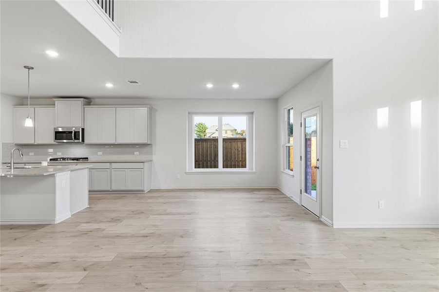 Kitchen with hanging light fixtures, white cabinets, stainless steel microwave, recessed lighting, and backsplash