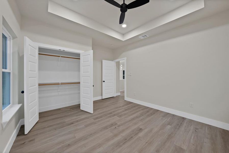Unfurnished bedroom with a raised ceiling, light wood finished floors, a ceiling fan, a closet, and recessed lighting
