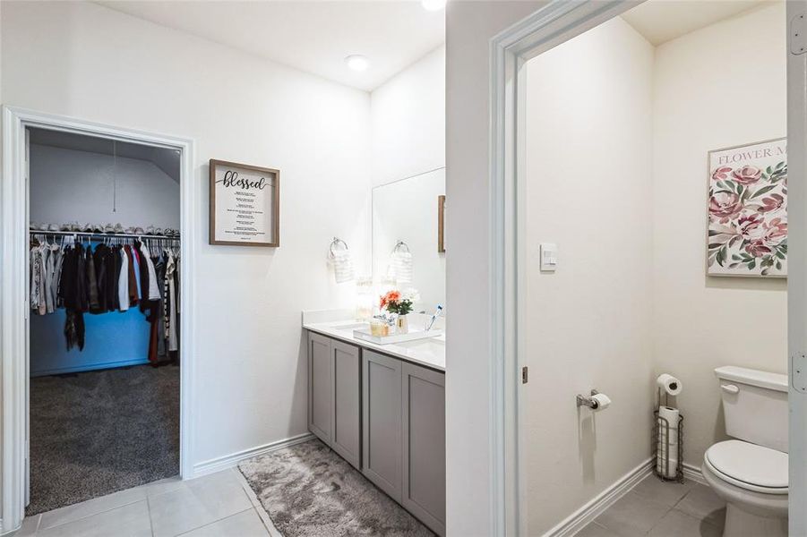 Full bath featuring toilet, baseboards, tile patterned floors, double vanity, and a walk in closet