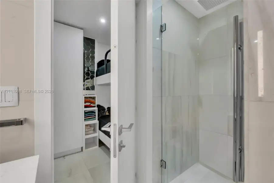 Shower enclosure featuring a seamless glass door, large-format polished wall tiling, and a vertical chrome hardware fixture Shower enclosure featuring a seamless glass door, large-format polished wall tiling, and a vertical chrome hardware fixture