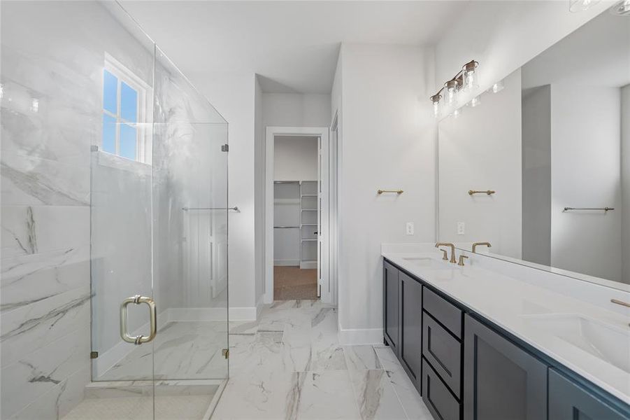 Full bathroom featuring double vanity, a walk in closet, a marble finish shower, and light marble finish flooring