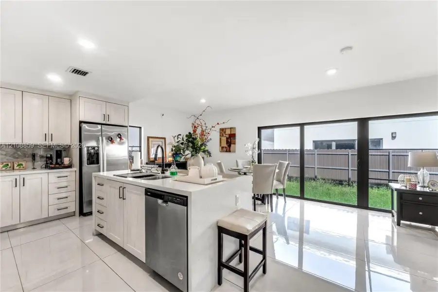 Kitchen featuring light-finish cabinetry, stone-surface countertops, center island with integrated stainless steel appliances, and large-format tile flooring