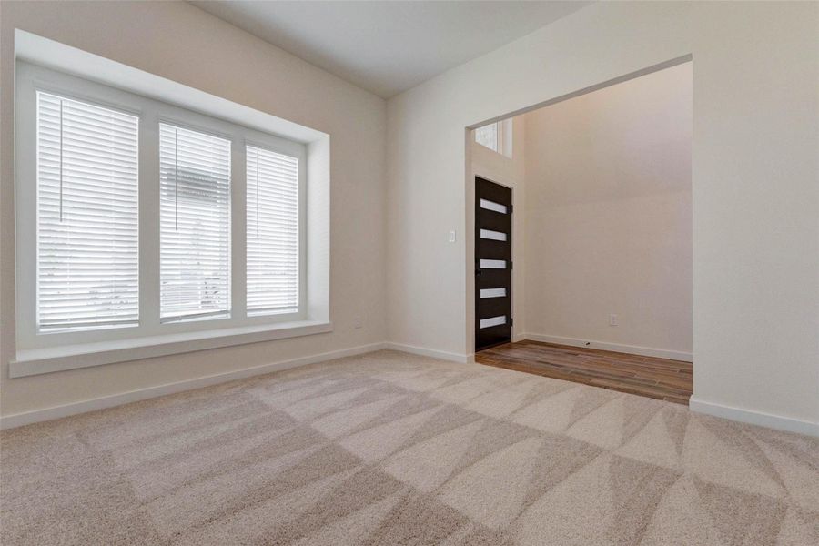 This spacious front living area is filled with natural light from large windows, creating an airy and comfortable environment. Perfect for relaxing or entertaining, the room offers flexible use and seamlessly connects to the entryway. The soft carpet underfoot and neutral palette provide a blank canvas, allowing future homeowners to easily personalize the space to suit their lifestyle.