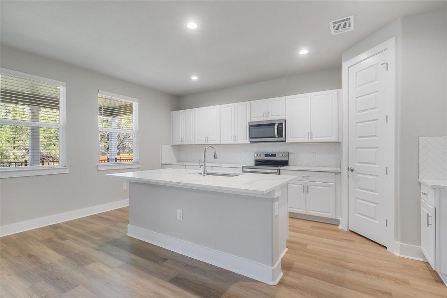Modern white kitchen with natural lighting, quartz countertops, sleek cabinetry, stainless appliances, recessed lighting, large center island, pantry, and modern backsplash design. Modern white kitchen with natural lighting, quartz countertops, sleek cabinetry, stainless appliances, recessed lighting, large center island, pantry, and modern backsplash design.