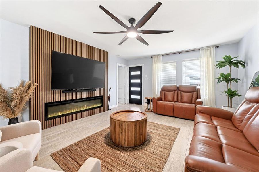 Living area featuring a slat wood accent wall with an integrated electric fireplace, tile flooring, and a contemporary ceiling fan