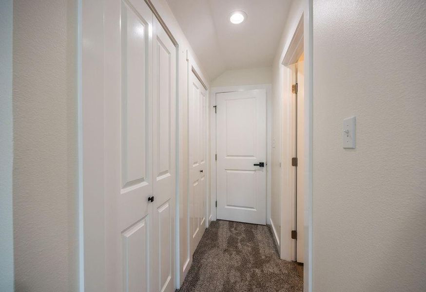 Hallway with dark colored carpet, a textured wall, and recessed lighting
