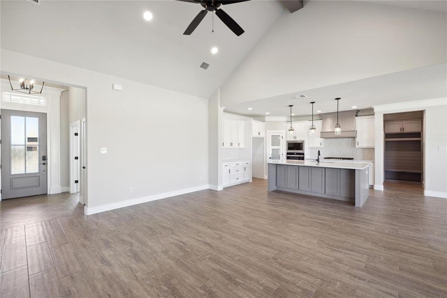 Unfurnished living room with high vaulted ceiling, wood-type flooring, and ceiling fan with notable chandelier