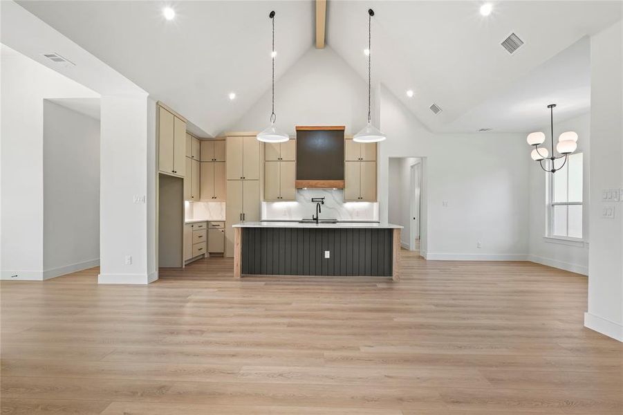 Kitchen with open floor plan, hanging light fixtures, beamed ceiling, an island with sink, and light wood-style flooring Kitchen with open floor plan, hanging light fixtures, beamed ceiling, an island with sink, and light wood-style flooring