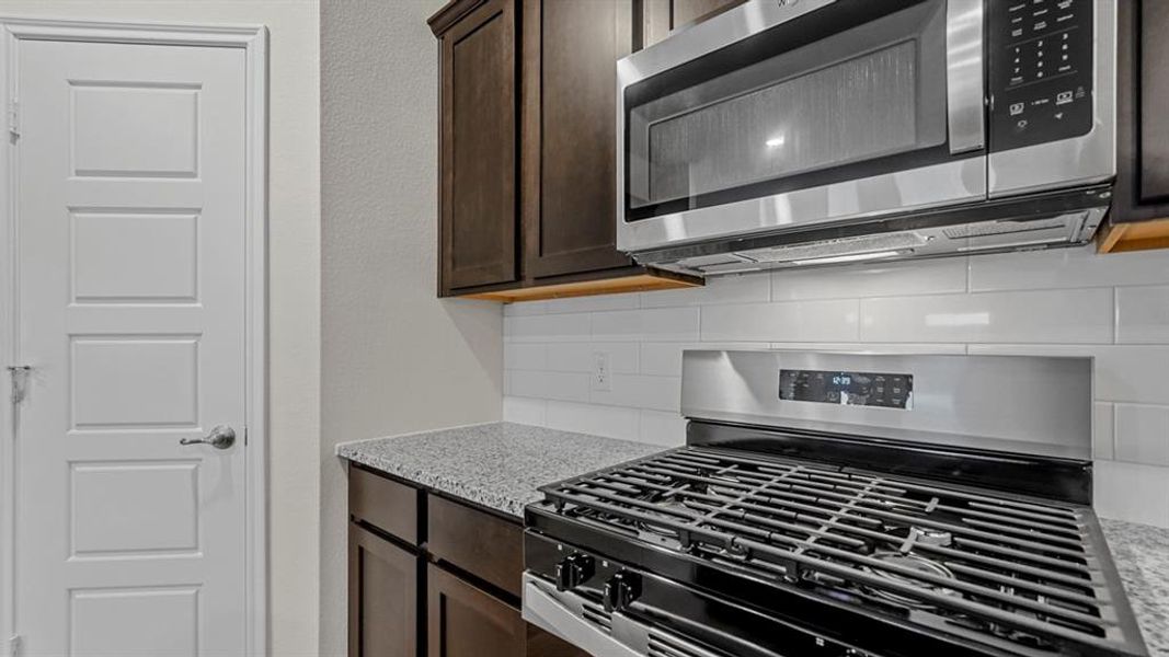 Kitchen featuring a gas range, over-the-range microwave, dark wood cabinetry, speckled countertops, and a white subway tile backsplash