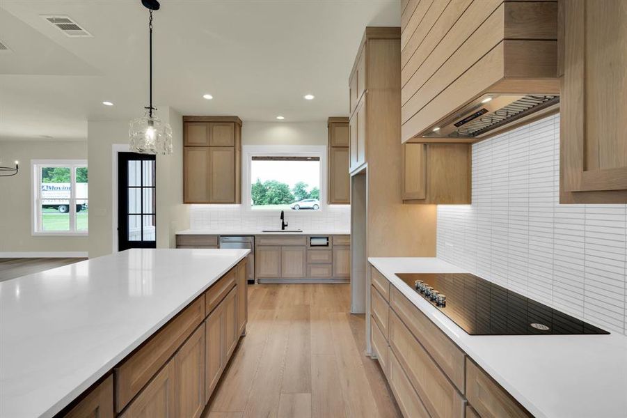 Kitchen with hanging light fixtures, a wealth of natural light, light hardwood / wood-style floors, backsplash, and premium range hood