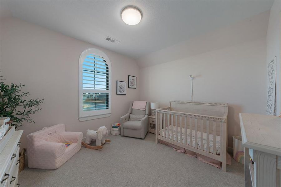 Bedroom with vaulted ceiling, a nursery area, carpet, and visible vents