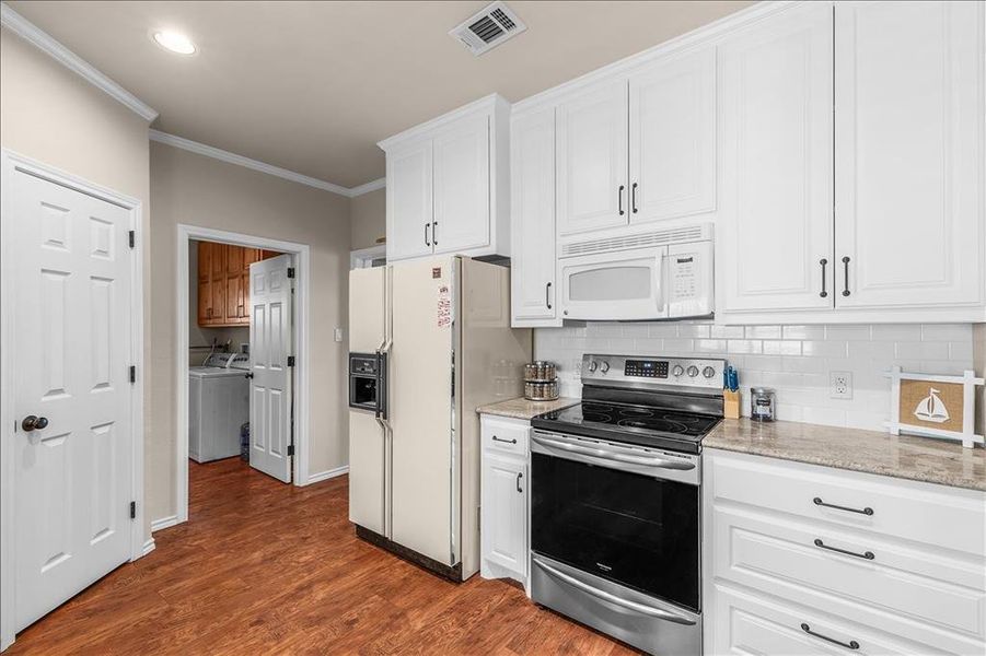 Kitchen with white appliances, white cabinets, crown molding, dark wood-type flooring, and light stone countertops