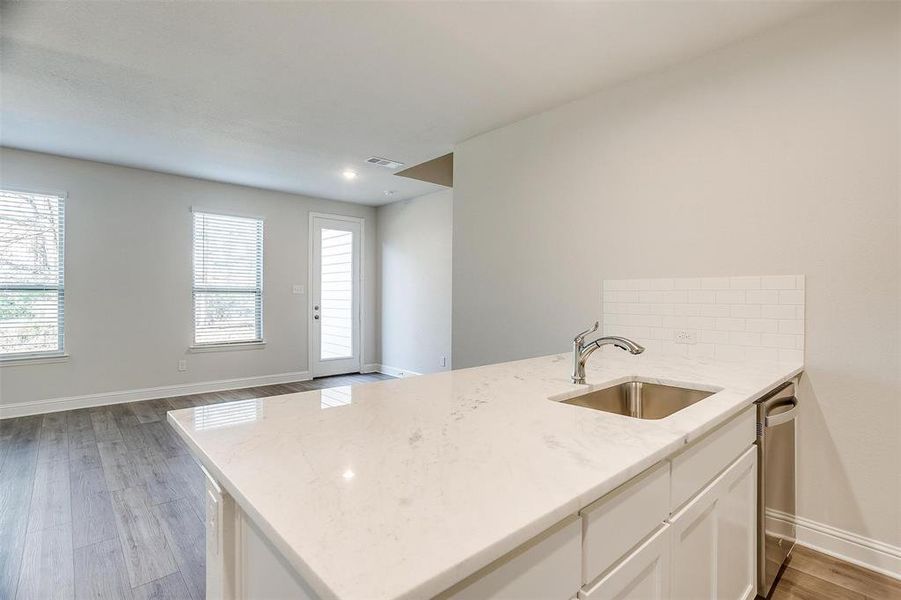 Kitchen featuring dishwasher, light stone counters, a sink, and visible vents