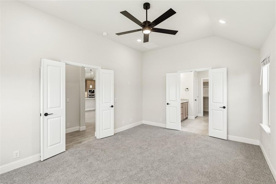 Empty master bedroom with gray carpet, ceiling fan, vaulted ceiling, and doors leading to bathroom and walk-in closet