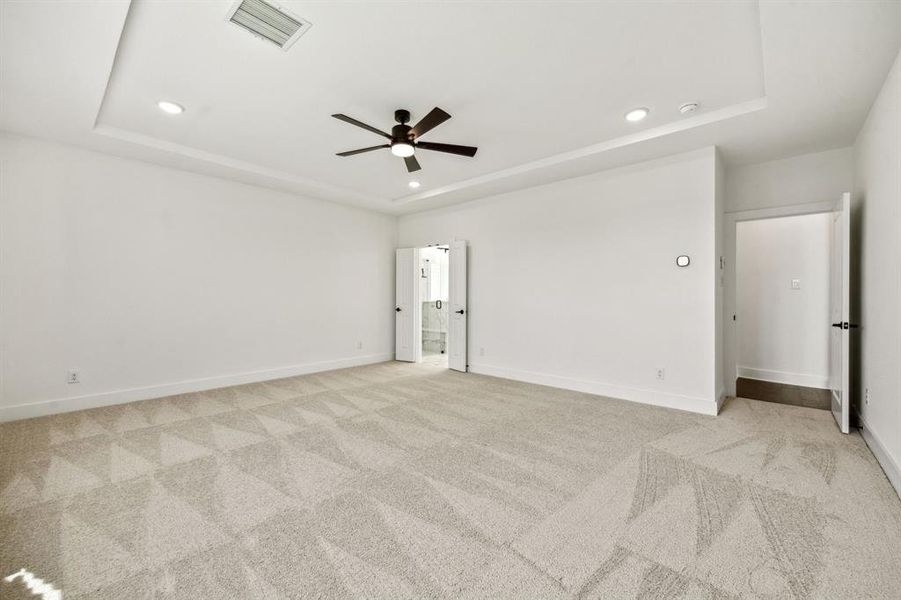 Empty room featuring a raised ceiling, ceiling fan, and light carpet