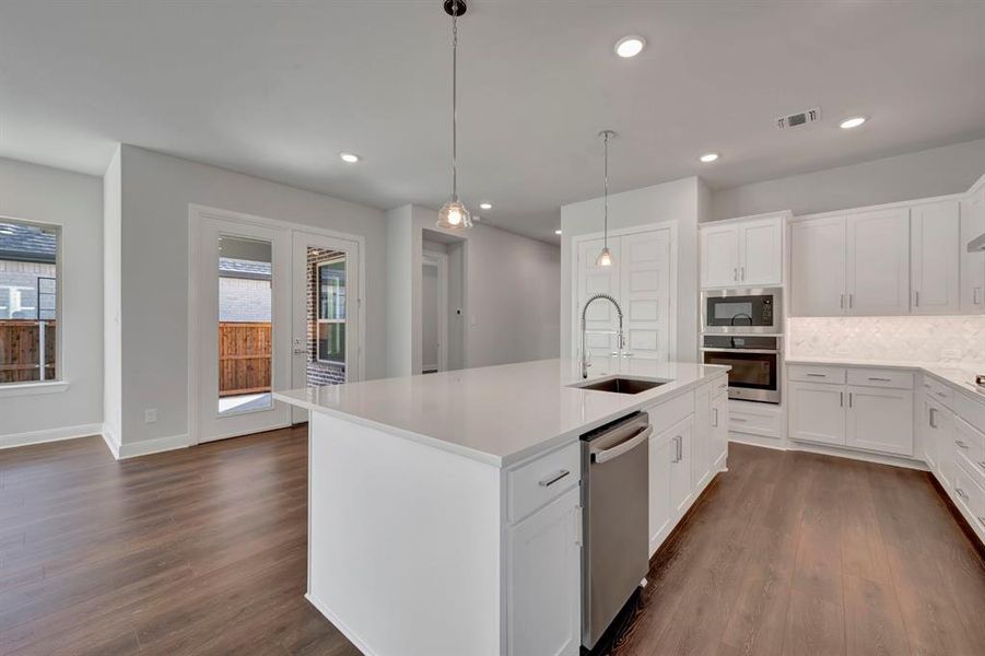 Kitchen with stainless steel appliances, white cabinets, backsplash, pendant lighting, and an island with sink