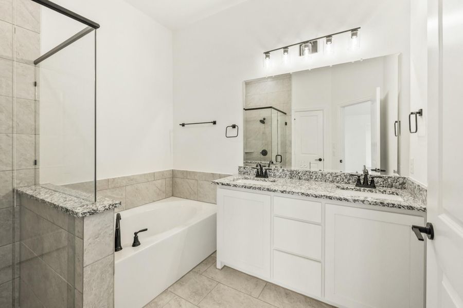 Bathroom with double vanity, granite countertops, soaking tub, and glass shower with gray tile