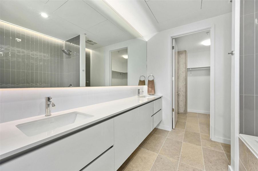 The second bathroom showcases a dual vanity with sleek white cabinets, providing ample storage & a modern aesthetic plus a large horizontal mirror, enhancing the spacious feel and functionality of the area. The second bathroom showcases a dual vanity with sleek white cabinets, providing ample storage & a modern aesthetic plus a large horizontal mirror, enhancing the spacious feel and functionality of the area.