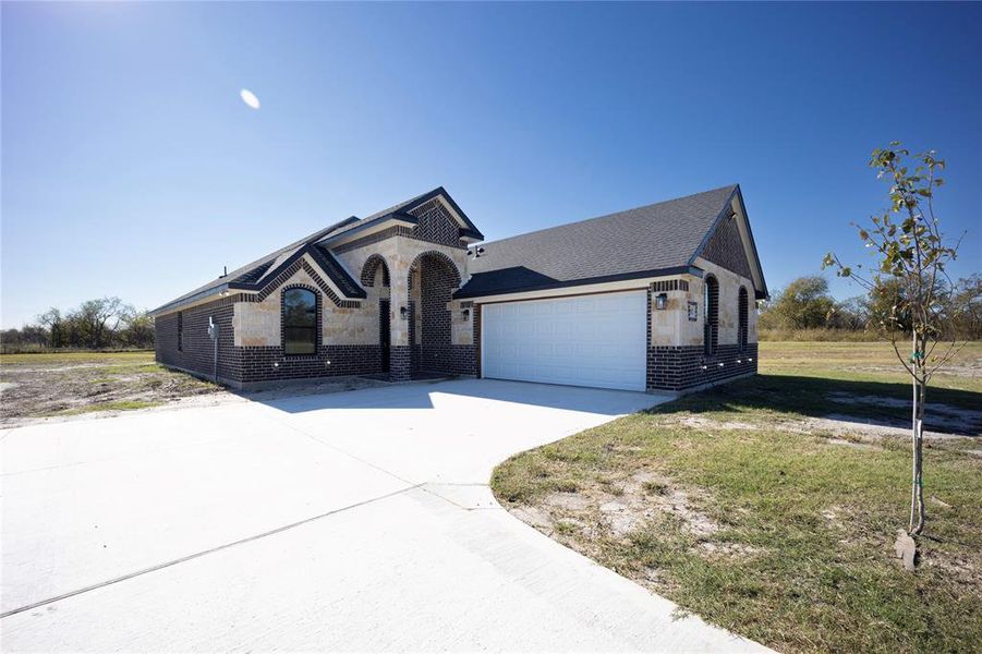 View of front of property attached garage, a front lawn, and stone