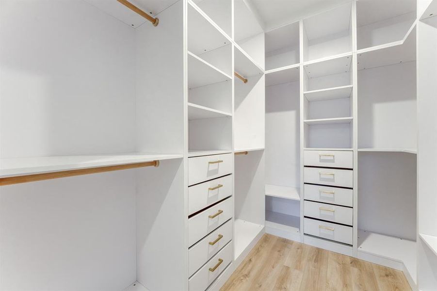 Huge luxurious custom built, walk-in closet with custom cabinetry, drawers, and gold accented hardware.