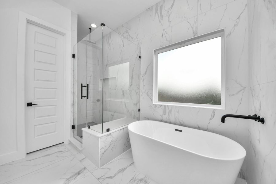 This modern bathroom features elegant marble walls and flooring, a sleek freestanding bathtub, and a spacious glass-enclosed shower. It offers a clean, luxurious design with a large frosted window for natural light.