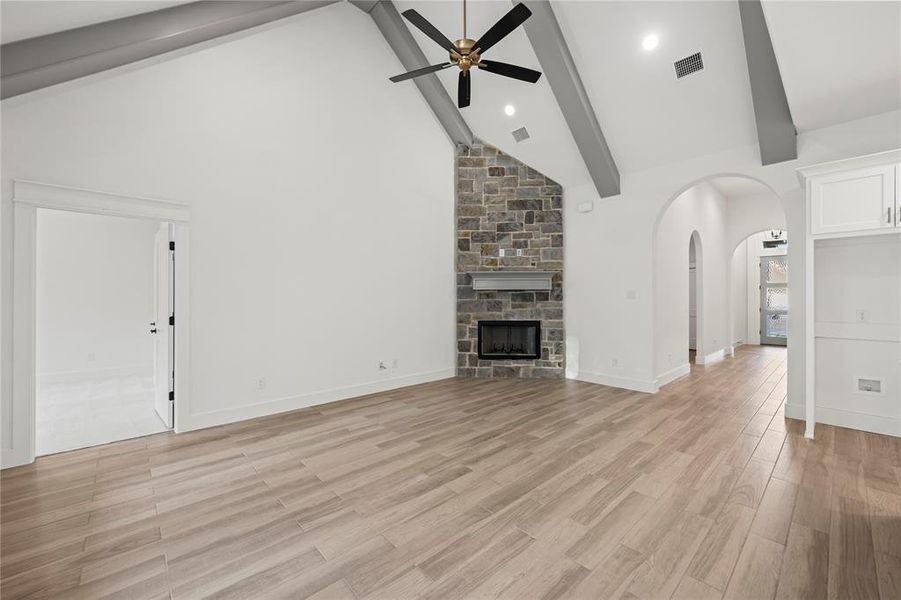 Unfurnished living room featuring light wood-type flooring, beamed ceiling, a stone fireplace, arched walkways, and high vaulted ceiling