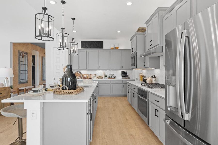 Kitchen featuring stainless steel appliances, a center island with sink, a kitchen breakfast bar, and gray cabinetry