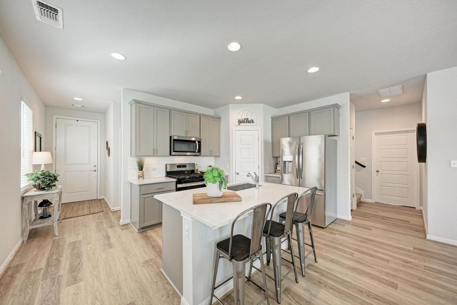 Kitchen featuring stainless steel appliances, gray cabinets, a kitchen breakfast bar, light wood-type flooring, and recessed lighting