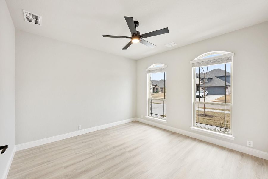 Empty bedroom with light wood floors, black ceiling fan, and two arched windows overlooking a neighborhood street Empty bedroom with light wood floors, black ceiling fan, and two arched windows overlooking a neighborhood street