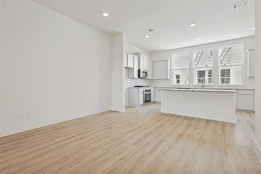 Open concept living area featuring light wood flooring, recessed lighting, and a kitchen with white cabinetry, stainless steel appliances, and a central island with a granite countertop