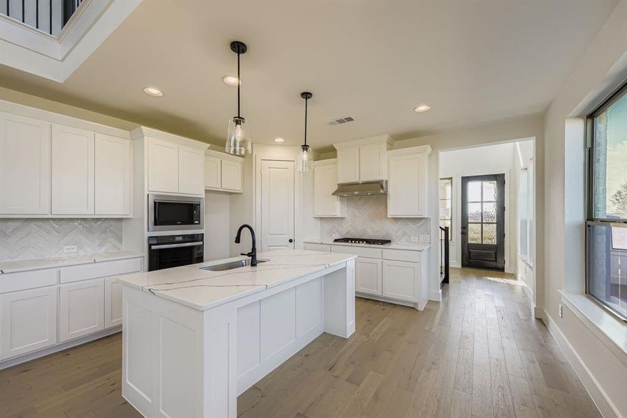 Kitchen with appliances with stainless steel finishes, white cabinets, pendant lighting, an island with sink, and light wood-style floors