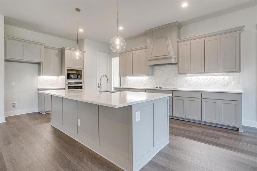 Kitchen with tasteful backsplash, sink, a center island with sink, custom exhaust hood, and hardwood / wood-style flooring