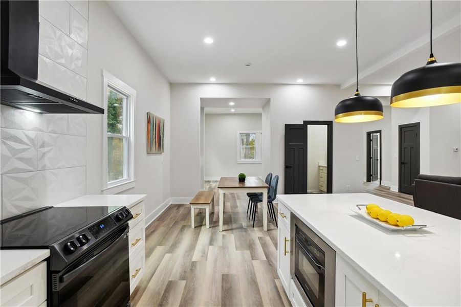 Kitchen with hanging light fixtures, wall chimney range hood, black range with electric stovetop, Luxury Vinyl Plank flooring, and white cabinetry