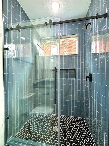 Showcasing the attractive shower area featuring floor-to-ceiling tiled walls enclosed by a glass door.