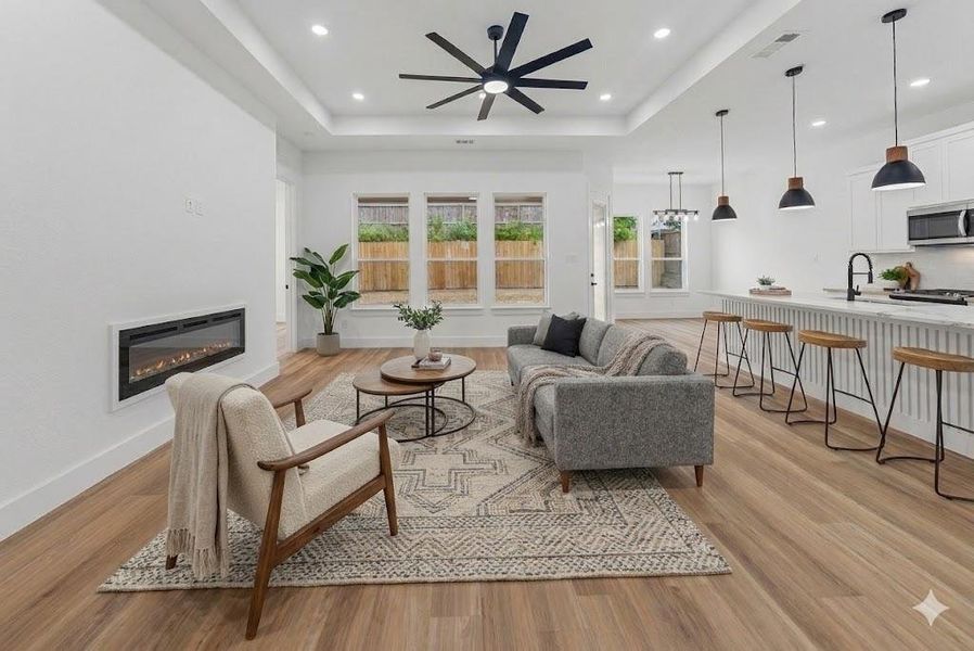 Virtually Staged - Open-concept living area featuring wood-finish flooring, a linear electric fireplace, a tray ceiling with a ceiling fan, recessed lighting, and large windows Virtually Staged - Open-concept living area featuring wood-finish flooring, a linear electric fireplace, a tray ceiling with a ceiling fan, recessed lighting, and large windows