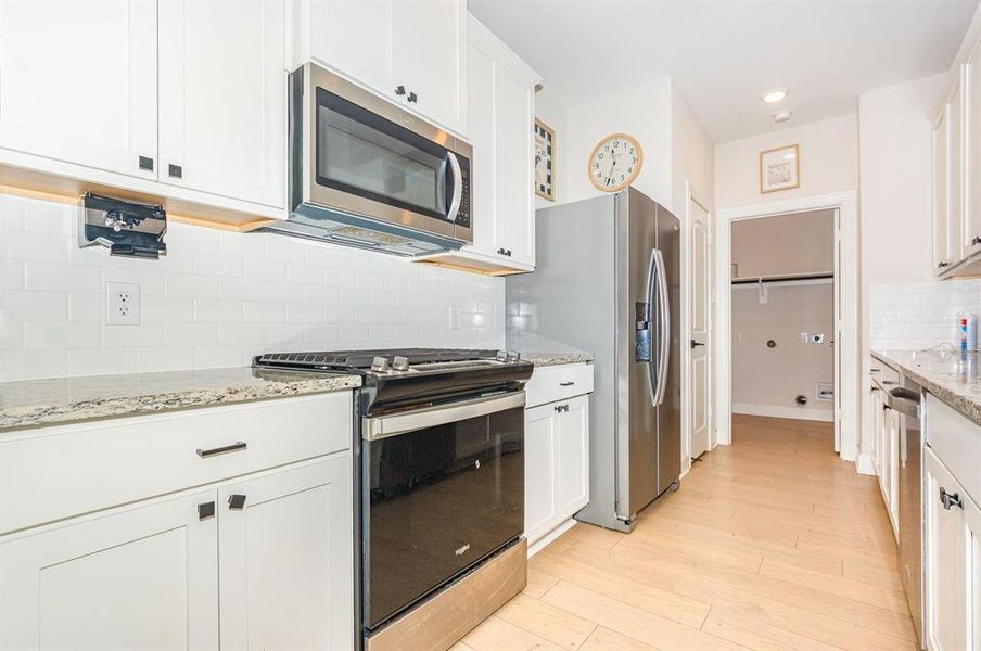 Kitchen featuring stainless steel appliances, decorative backsplash, white cabinetry, light stone counters, and light wood-type flooring Kitchen featuring stainless steel appliances, decorative backsplash, white cabinetry, light stone counters, and light wood-type flooring