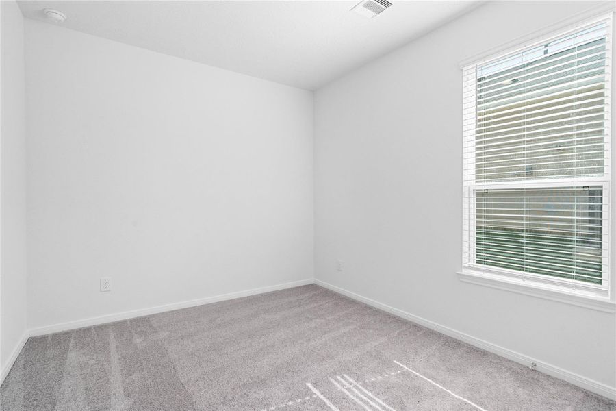 Light-filled secondary bedroom complete with cozy carpet flooring, ample closet space, and a large window with fitted blinds.