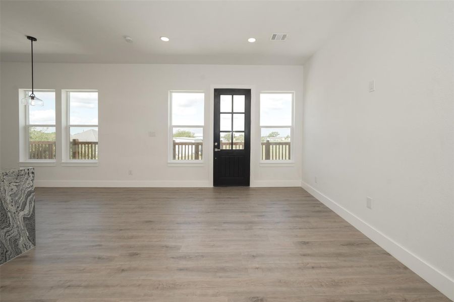 This bright, open room features light wood flooring and fresh white walls, creating a modern and airy feel. It includes large windows for natural light and a black door leading to an outdoor deck, perfect for enjoying the view.