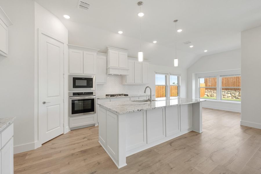 White kitchen with large island, granite countertops, stainless steel appliances, and light wood floors White kitchen with large island, granite countertops, stainless steel appliances, and light wood floors