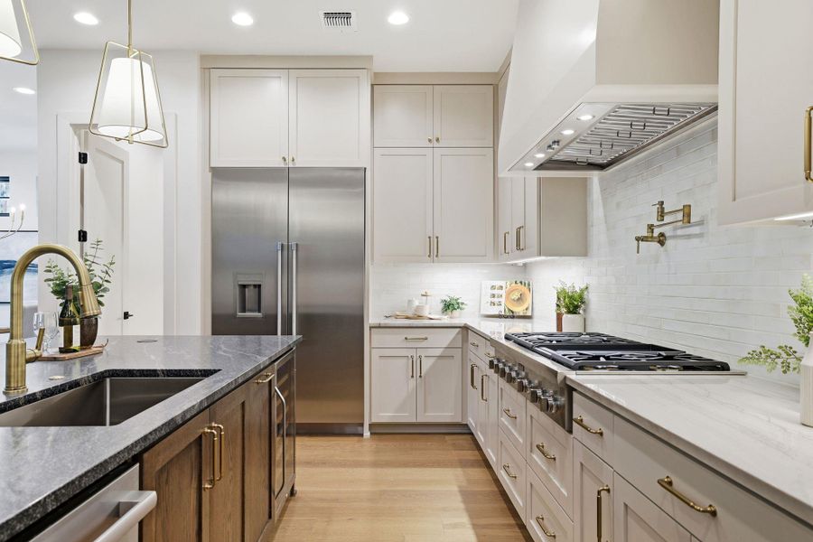 Kitchen featuring dark stone countertops, custom exhaust hood, appliances with stainless steel finishes, light wood-style flooring, and recessed lighting