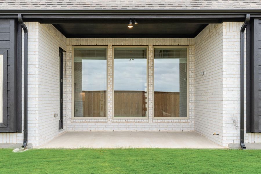 Covered back patio with white brick exterior, large windows, and concrete slab overlooking green lawn