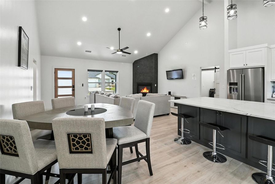 Dining space featuring high vaulted ceiling, recessed lighting, a ceiling fan, a fireplace, and light wood-type flooring