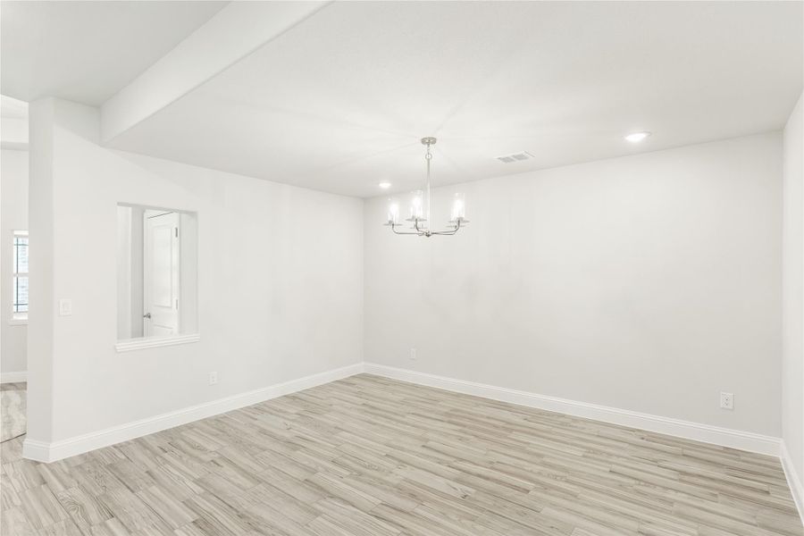 Empty dining room with light wood floors, white walls, and a modern chandelier