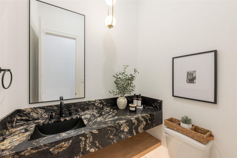 A powder room composed around a single piece of stone. Dramatic black-and-gold veining wraps the counter and integrated splash like a painting: then every other element steps back: matte-black sink, matte-black faucet, black-framed mirror. Only the brass pendant is allowed to warm the room.