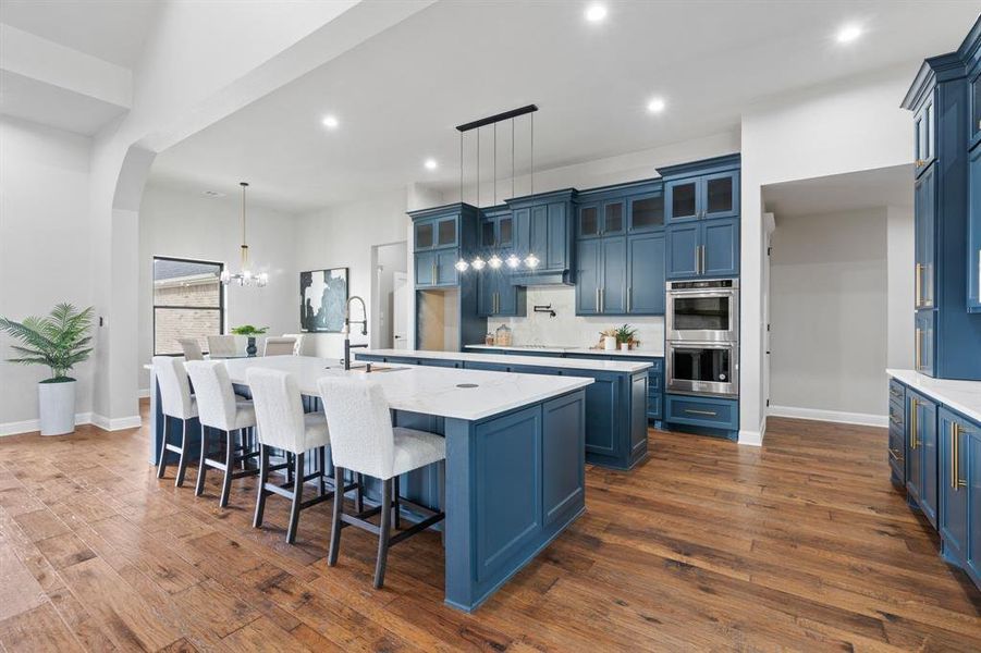 Kitchen featuring decorative light fixtures, double oven, a kitchen island with sink, and blue cabinets
