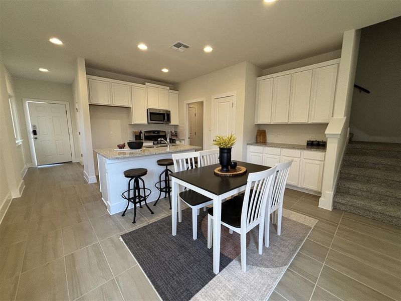 Kitchen featuring light tile patterned floors, stainless steel appliances, a kitchen island with sink, light stone countertops, and white cabinets