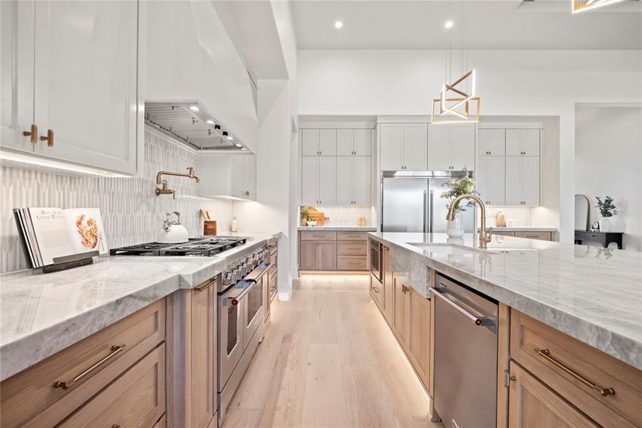 Kitchen featuring light stone countertops, high end appliances, premium range hood, decorative backsplash, and light wood finished floors
