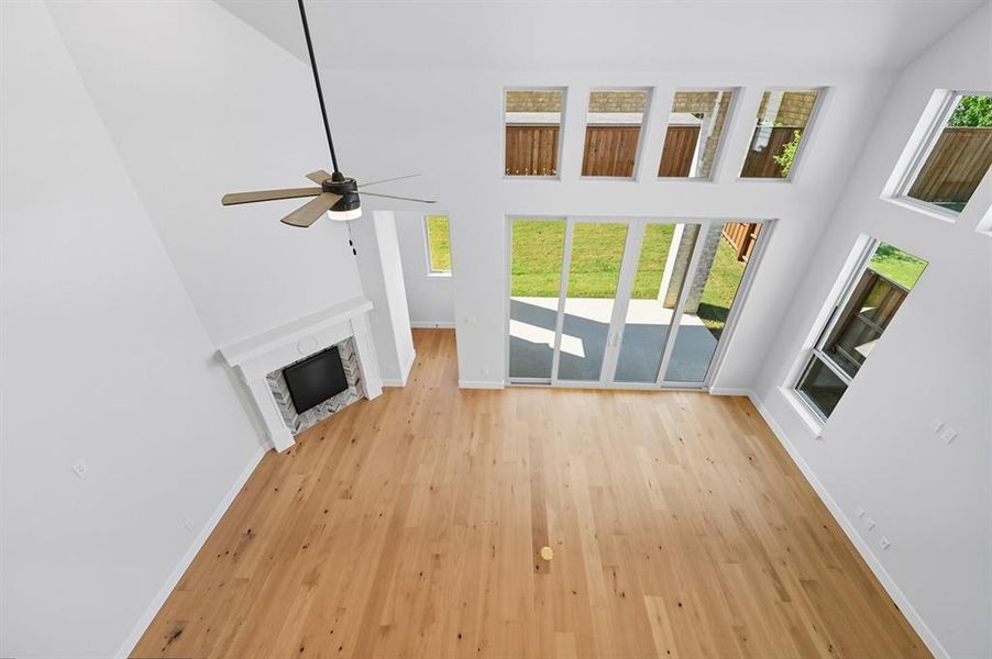 Unfurnished living room featuring light wood-style floors, a stone fireplace, a towering ceiling, and ceiling fan