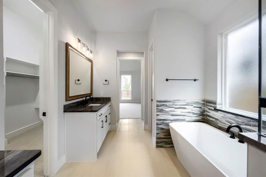 Bathroom featuring a freestanding soaking tub, a single vanity with a dark countertop and undermount sink, and light-toned tile flooring